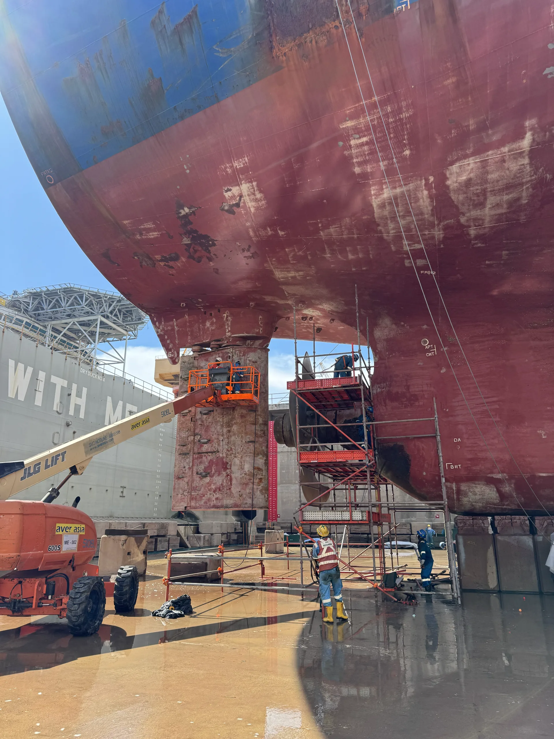 Crew on lifts preparing the hull of a ship in drydock